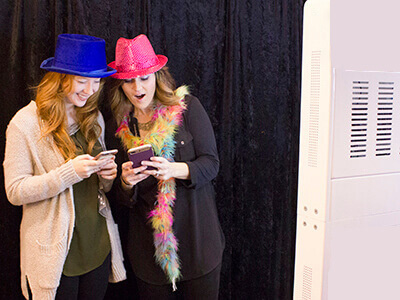 two friends share photos on their smart phones outside the photo booth